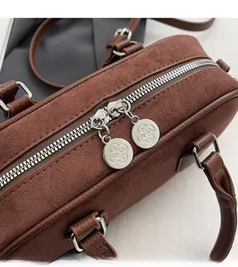 Detail of dual silver metal zippers and round clover engraved pullers on a suede handbag