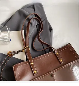 Detail of brown leather tote bag handle with golden studs and decorative side cords