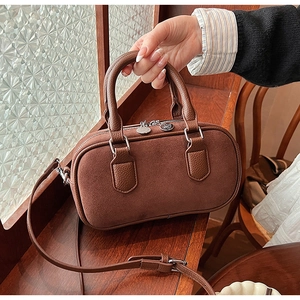Détail du sac bowling en daim marron vintage tenu à la main sur fond rétro élégant