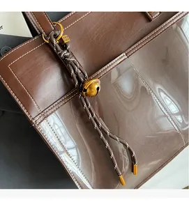 Detail of brown leather tote featuring clear PVC paneling and white stitching accents
