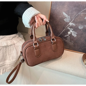 Gros plan sur un sac bowling rétro marron avec surpiqûres en daim et zip métallique