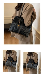 Detail of black PU tote bag featuring white stitching and a golden bell charm ornament