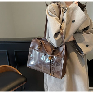 Detail of a brown leather and PVC tote bag with tassel charm worn by a model