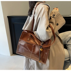 Detail of caramel brown shoulder bag with contrast stitching and golden bell decor