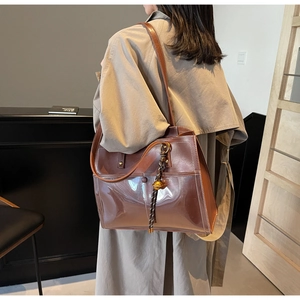 Close-up of brown PVC tote bag featuring contrast stitching and golden bell charm detail