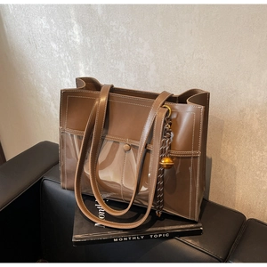 Detail of a brown leather tote with a transparent PVC front pocket and gold bell charm