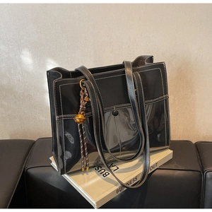 Detail of black leather tote bag with white stitching and decorative gold bell charm