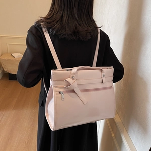 Pink faux leather commuter backpack with top handle and knot detail in a cozy home setting
