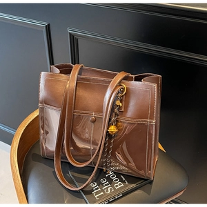 Close-up of brown leather and PVC tote bag with white contrast stitching and gold charm