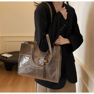 Close-up of brown tote bag with PVC panels and gold sphere charm on black blazer