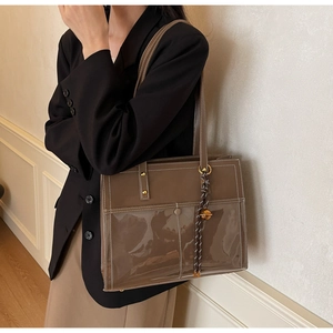 Detail of dark brown tote bag featuring a transparent PVC front pocket and white stitching