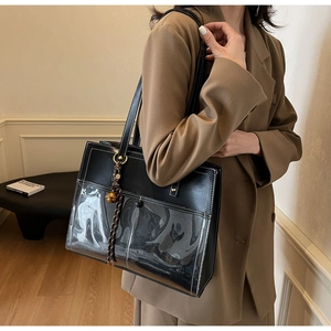 Detail of black tote bag with transparent PVC front pocket and woven charm detail