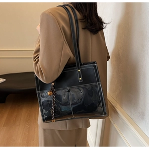 Detail view of large black leather tote bag with white stitching and hanging charm ornament