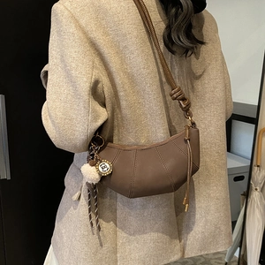 Brown pleated crescent shoulder bag with plush charm and metal tag detail for women