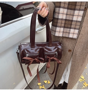 Détail d'un sac cylindrique chocolat avec nœuds en satin et poches zippées avant