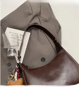 Detail of a dark brown leather underarm bag with a cute bear charm on a grey blazer