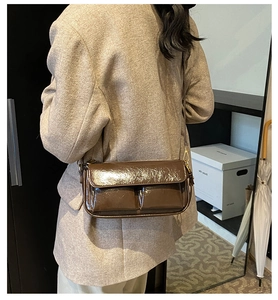 Detailed close-up of brown patent leather shoulder bag with gold zipper and dual pockets