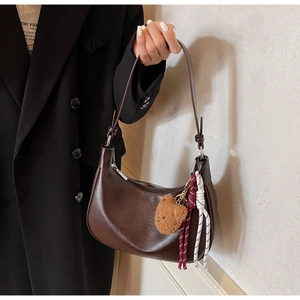 Detail of dark brown hobo bag featuring a plush bear charm and sleek leather texture