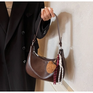 Detail of dark brown leather hobo bag featuring a cute plush bear charm and woven cord