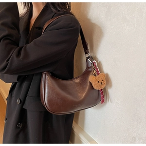 Detail of dark brown crescent underarm bag with cute plush bear charm on a black coat