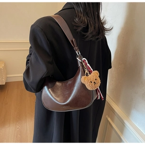 Close-up of a dark brown glossy leather hobo bag with a cute plush bear charm on a model
