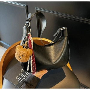 Detail of black matte leather hobo bag with a brown plush bear charm and woven tassel