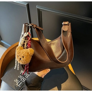 Detail of dark brown hobo shoulder bag with glossy texture and teddy bear charm