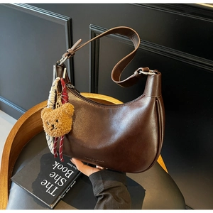 Detailed macro view of dark brown leather crescent bag with a cute plush bear pendant