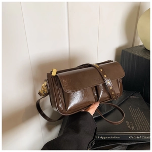 Detail of dark brown polished leather shoulder bag with gold rivets and Paris lettering