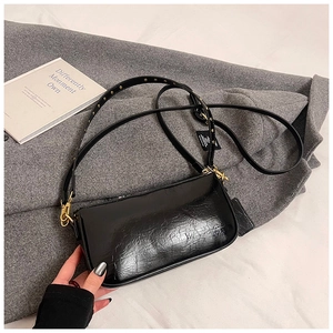Detail of black glossy crinkled leather underarm bag with gold rivets and spring buckle