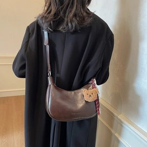 Brown crescent shoulder bag with plush bear charm and checkered scarf accessory
