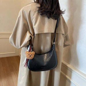 Fashionable black hobo bag with teddy bear pendant worn by a model in a beige coat
