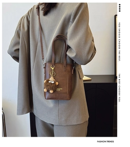 Brown leather bucket bag with plush charm and shoulder strap shown on a model