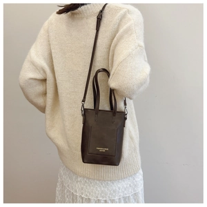 Close-up of a vintage dark brown leather mini tote bag styled on a white lace skirt dress