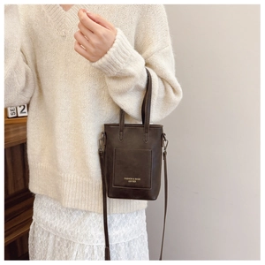 Close-up of a brown mini bucket bag with gold lettering and top handle on a white sweater