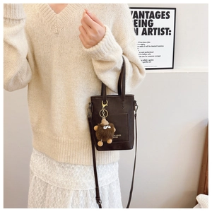 Detail of dark brown leather handbag with a plush monster charm and slim shoulder strap