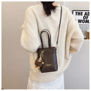 Detail of dark brown leather mini tote bag with cute plush monster charm on a white sweater