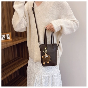 Mini brown leather tote bag with plush charm and shoulder strap in a lifestyle setting