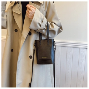 Detail of a chic black leather bucket bag showing the fashion logo and strap on a beige coat