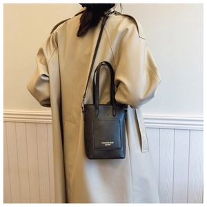 Detail of a black leather crossbody bag with golden fashion lettering on khaki trench coat