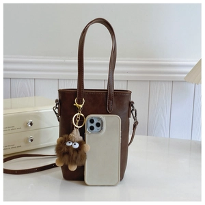 Brown leather tote bag detail with cute plush charm and adjustable shoulder strap