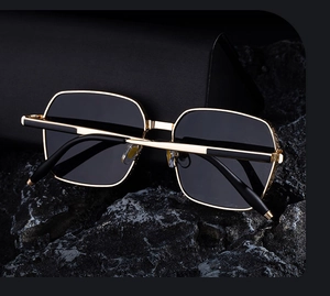 Vue détaillée de lunettes de soleil carrées à monture dorée et verres noirs sur pierre