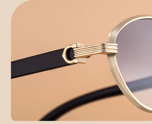 Detail of oval sunglasses featuring a gold C-shape hinge on black metal frame
