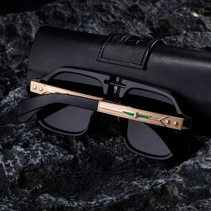 Detail of square black sunglasses with gold metal temples and star rivet on rock