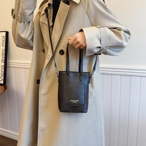 Minimalist black leather mini tote bag with gold lettering shown on beige trench coat