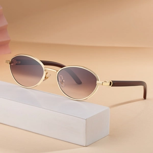 Oval fashion sunglasses with gradient lenses and wood grain temples on a beige stand