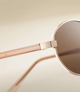 Close-up of golden metal sunglasses frame with intricate cross-hatched lattice engraving