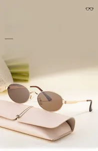 Détail de lunettes de soleil ovales dorées avec un étui en cuir texturé rose clair