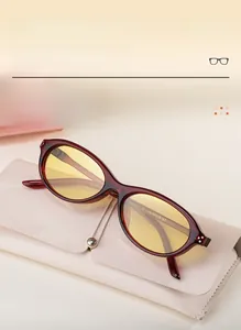 Détail de lunettes œil-de-chat bordeaux avec verres jaunes sur un étui en cuir blanc