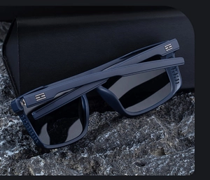 Close-up of square navy sunglasses with silver H-hinge detail on dark natural rock